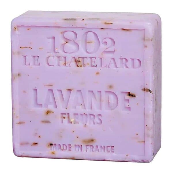 Un săpun pătrat, de culoarea lavandei, cu pete de maro servește ca un exfoliant blând. Gravat cu textul „1802 Le Chatelard Lavande Fleurs Made in France”, acest exfoliant Săpun Natural de Marseille cu Flori de Lavandă prezintă eleganță și calitate.