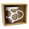 Ceașcă pentru Ceai cu Infuzor, Mandala Roșie este o cană de ceai din ceramică albă, cu un model floral vibrant Mandala Roșie în roșu, verde și galben. Vine cu un mâner mare, un capac de infuzor asortat și o lingură mică de metal, toate afișate elegant într-o cutie de carton.