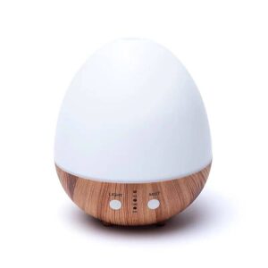 Difuzorul de Aromă Oval Alb Natural USB este un difuzor de uleiuri esențiale cu ultrasunete, cu un blat neted, alb și o bază texturată cu granule de lemn. Baza include două butoane etichetate „Light” și „Mist”, cu mici lumini indicatoare între ele. În plus, oferă opțiuni convenabile de alimentare prin portul său USB.