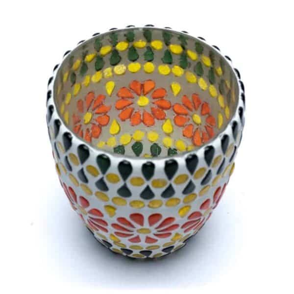 Un suport de lumânări din ceramică vibrant, cu formă rotundă, împodobit cu un design de flori portocalii și galbene și frunze verzi. Suportul pentru Lumânări din Sticlă Mozaic Verde/Galben are un fundal alb accentuat de chenare punctate alb-negru în jurul vârfului.