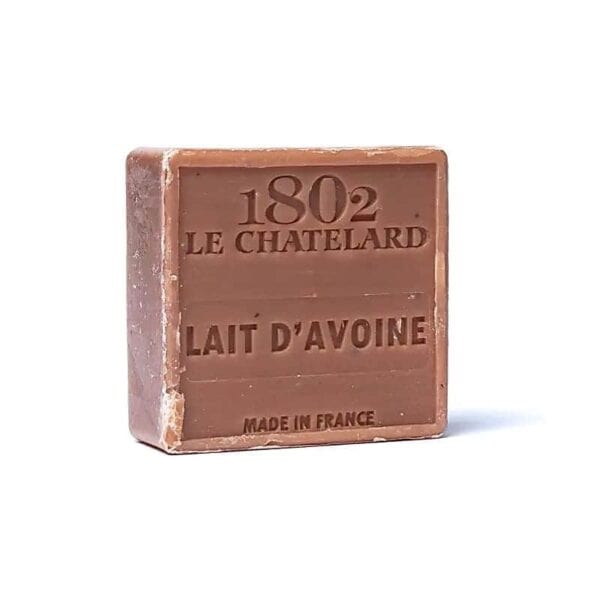 O tabletă pătrată de săpun maro Săpun Natural Marseilles cu Lapte de Ovăz cu text în relief cu „1802 Le Chatelard Lait D'Avoine, Made in France” pe suprafața sa frontală. Săpunul, cunoscut pentru că este un săpun natural din Marsilia, este ușor purtat pe margini și se așează pe un fundal alb simplu.