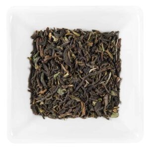 Un vas pătrat alb umplut cu ceai din frunze vrac Darjeeling Prima Recoltare FTGFOP1. Frunzele de Darjeeling verde închis și maro par uscate și ușor ondulate, indicând o calitate premium. Culorile contrastante ale frunzelor și preparatului Prima Recoltare creează o prezentare atrăgătoare din punct de vedere vizual.