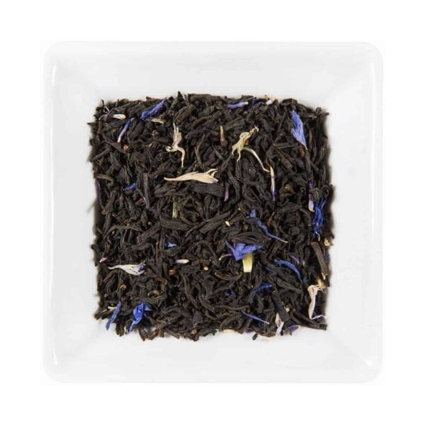 Un fel de mâncare albă pătrată umplută cu ceai „Earl Gray cu Flori de Albăstrele”, care prezintă un amestec de Earl Grey din frunze vrac cu petale de Flori de Albăstrele violet vibrant și albe. Amestecul prezintă un contrast izbitor între frunzele de ceai închis la culoare și petalele strălucitoare și colorate.