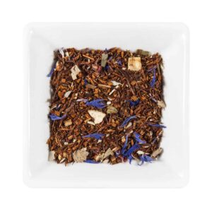 Un fel de mâncare pătrată albă care conține ceai exotic din frunze vrac, cu un amestec de frunze de rooibos maro-roșcat, petale de flori violet și bucăți mici de fructe uscate.